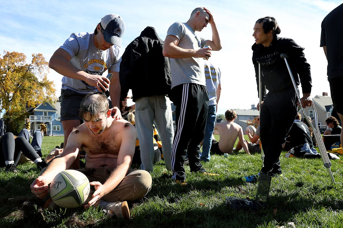 Current student and rugby player Brody Herrick shaves fellow student and rugby player Aidan Helgeson’s head as part of a long-standing, annual tradition of the current student vs. alumni game while others watch during Homecoming Weekend. Photo by Jamie Cotten / Colorado College